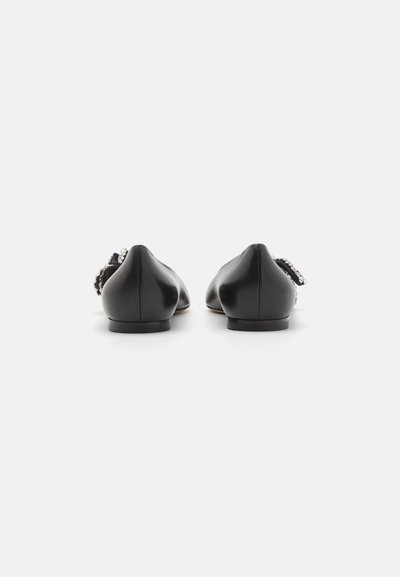 Mocasines de cuero negro con tacón bajo, punta en forma de almendra y detalle decorativo en la parte posterior que presenta acentos de cristal.
