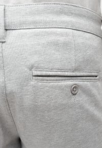 Pantaloni gri deschis cu material texturat ce prezintă un model în carouri, un buzunar posterior cu margine pipă și un detaliu cu nasture.