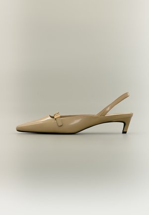 Bézs lakkozott bőr slingback kissarkú cipő hegyes orral és kis csatos pánttal, semleges háttéren.