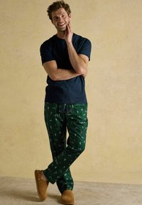 Jūras spēku īsām piedurknēm krekls, zaļas pidžamas bikses ar rotaļīgām rakstām, un brūni čības. Gluda tekstūra un brīvs piegriezums.