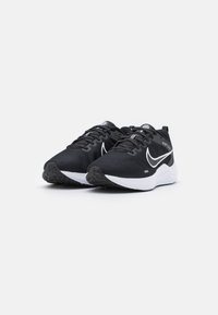 Scarpe da ginnastica nere con superiore testurizzato, logo swoosh bianco e suola bianca ammortizzata, con lacci neri e battistrada in gomma.