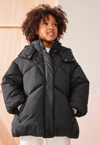 Schwarze gepolsterte Jacke mit hohem Kragen, Zickzack-Steppung und Knopfdetails. Verfügt über große Ärmel und seitliche Taschen für zusätzliche Wärme.