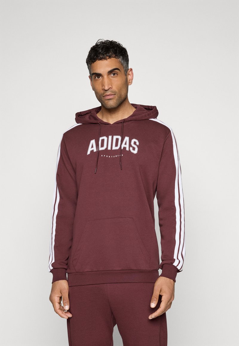 Sweatshirt à capuche bordeaux avec accents blancs et logo "ADIDAS" sur le devant. Dispose d'une capuche avec cordon de serrage et d'une poche kangourou sur le devant.