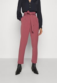 Hoge taille, roze op maat gemaakte broeken met een strikceintuur, met een gladde textuur en zakdetails, gecombineerd met een navy blouse met knopen en zwarte laarzen.