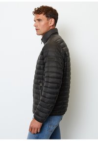 Chaqueta de abrigo negra con diseño acolchado, cuello alto y bolsillos con cremallera. Textura suave, ligera, con silueta ajustada.