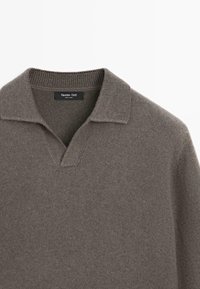 Brauner Strickpullover mit einem gerippten Kragen und einem tiefen V-Ausschnitt, innen im Kragen mit einem schwarzen Etikett mit weißem Text versehen.