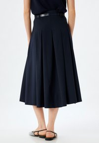 Gonna midi plissettata blu navy con fascia in vita aderente e una texture liscia. La parte posteriore presenta un accento di cintura nera e un silhouette svasata.