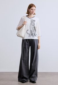 Λευκό τοπ με σχέδιο λεοπάρδαλης, άνετο γκρι παντελόνι φαρδιάς γραμμής και κρεμ τσάντα χειρός. Μαλακό ύφασμα με χαλαρή εφαρμογή και σφικτά τελειώματα στα μανίκια.