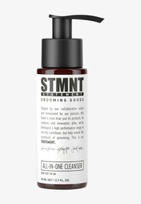 Bouteille en verre rouge avec un bouchon pompe noir. L'étiquette blanche présente un texte noir en gras : « STMNT GROOMING GOODS » et « ALL-IN-ONE CLEANSER ».