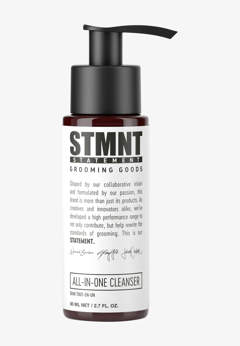 Bouteille en verre rouge avec un bouchon pompe noir. L'étiquette blanche présente un texte noir en gras : « STMNT GROOMING GOODS » et « ALL-IN-ONE CLEANSER ».