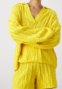 Gul stickad tvådelad outfit bestående av en v-ringad, oversized tröja med ett strukturerat mönster och matchande shorts.