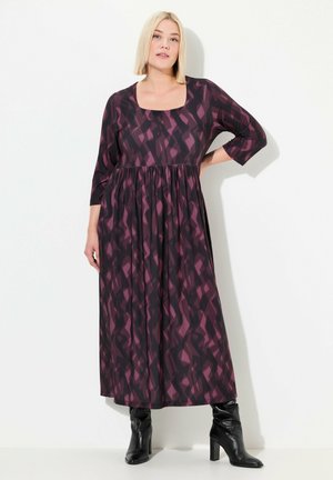 Robe maxi en tissu violet foncé avec des motifs géométriques dans des nuances plus claires. Présente un décolleté carré et des manches trois-quarts, assortie à des bottes noires jusqu'aux genoux.