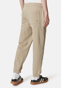 Pantaloni jogger in cotone beige con elastico in vita, due tasche posteriori, vestibilità slim e orli cuffiati. Presentano cuciture decorative su una gamba.