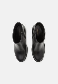 Botines de cuero negro con un acabado liso, cremalleras laterales, punta redondeada y un tacón bajo. El interior presenta el logo de la marca grabado.