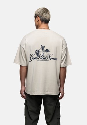 Beige oversized t-shirt featuring a printed design in dark blue on the back, with text "Good For Nothing" and decorative imagery.