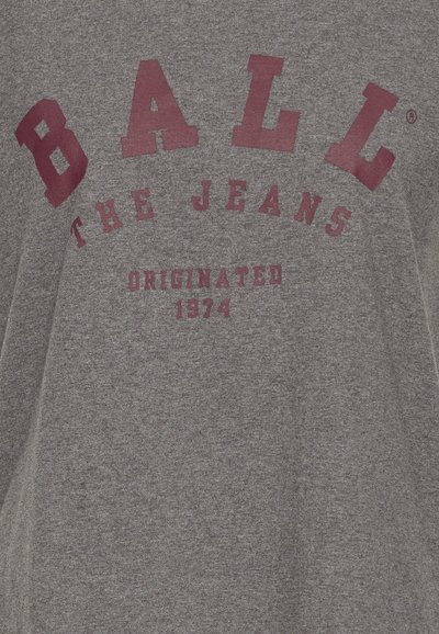 Grå t-shirt lavet af bomuld med rund halsudskæring. Har fede kastanjebrun bogstaver: "BALL," "THE JEANS," og "ORIGINATED 1974."