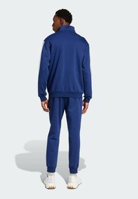 Jūras spēku sporta tērps ar rāvējslēdzēja jakas augstu apkakli, baltām sānu svītrām un atbilstošām biksēm. Izgatavots no mīksta, elastīga auduma.