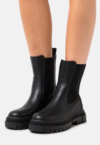Botas de cuero negro hasta el tobillo con paneles laterales elásticos, superficie texturizada, puntera redonda y suela de goma gruesa con un patrón de goma profundo.