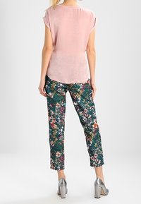 Top corto a maniche corte rosa chiaro, vista posteriore; abbinato a pantaloni attillati con motivo floreale in verde scuro, con vari colori, e tacchi argentati.