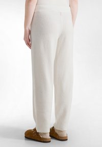 Witte fleece broeken met een ontspannen pasvorm, voorzien van een soepele tailleband en een zachte structuur. G.combineerd met bruine klompen en lichte sokken.