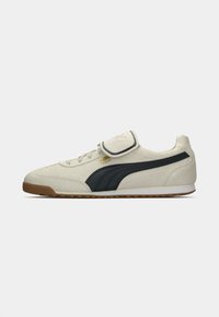 PUMA sneakers med en overdel i beige ruskind, sorte sidelister og en gummiydersål. Inkluderer en velcrorem.