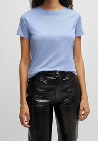 Ljusblå bomullströja med rund hals och korta ärmar, med en liten broderad "BOSS"-logga på bröstet. Kombinerad med svarta glänsande imitationläderbyxor.