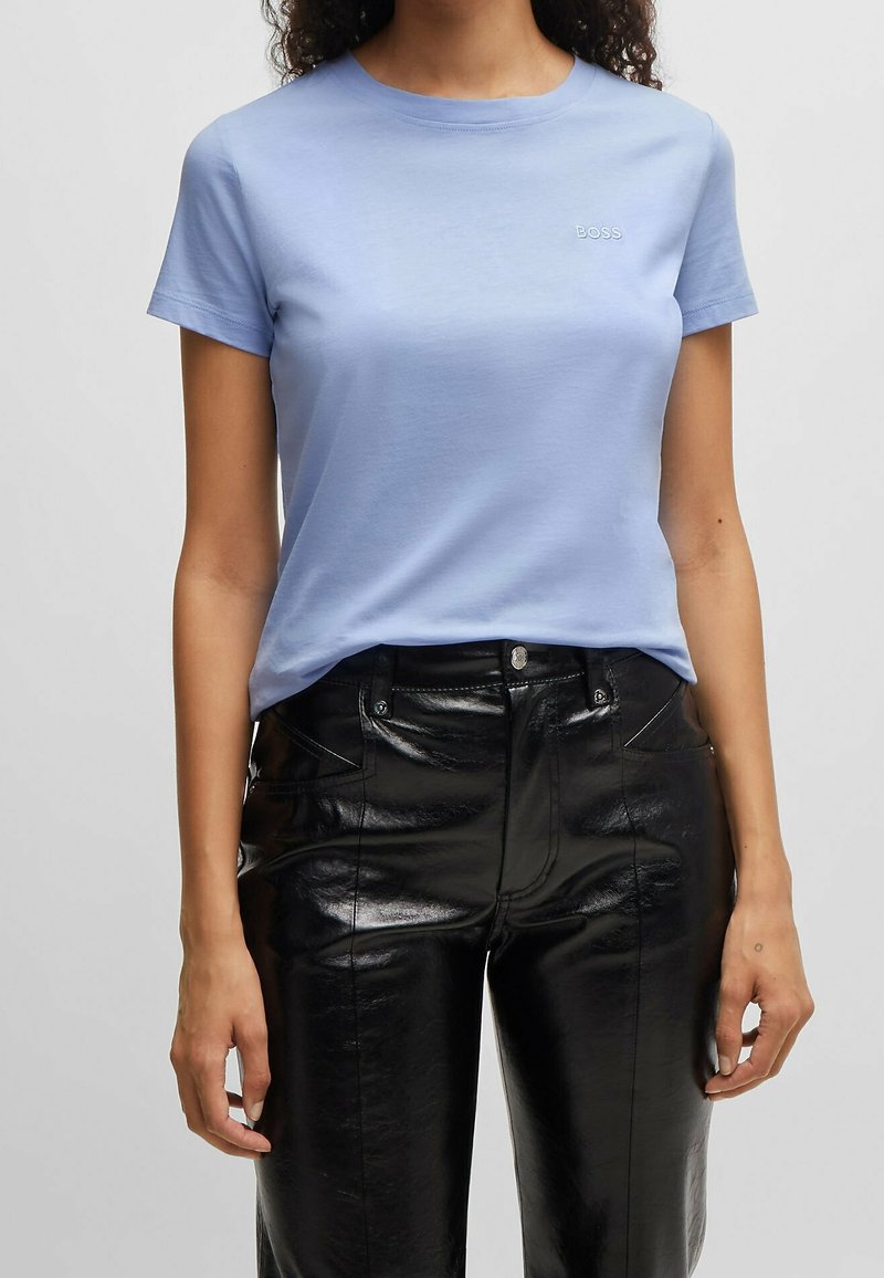 Ljusblå bomullströja med rund hals och korta ärmar, med en liten broderad "BOSS"-logga på bröstet. Kombinerad med svarta glänsande imitationläderbyxor.