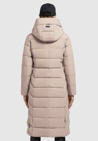 Gepolsterter langer Mantel in hellbeige mit Kapuze, der gestickte quadratische Muster und ein Etikett mit Logo an der Seite aufweist. Glattes, wasserabweisendes Material.