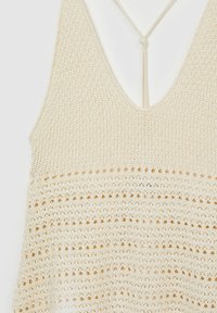 Haut sans manches en crochet couleur crème avec col en V et motifs tricotés texturés.