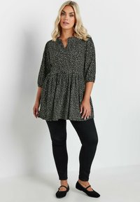 Tunic a pois bianco e nero con vita arricciata, maniche a tre quarti e scollatura a V, abbinata a jeans skinny neri e ballerine.