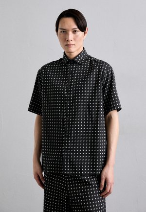 Chemise noire à manches courtes avec un motif blanc de petites formes, col boutonné, texture lisse et coupe décontractée, accompagnée de pantalons assortis.