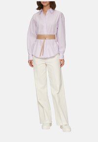 Helllila gestreifte Button-Down-Bluse mit einem gebundenen beigefarbenen Gürtel, kombiniert mit weiten weißen Hosen und klobigen weißen Sneakers, die geschichtete Texturen präsentieren.