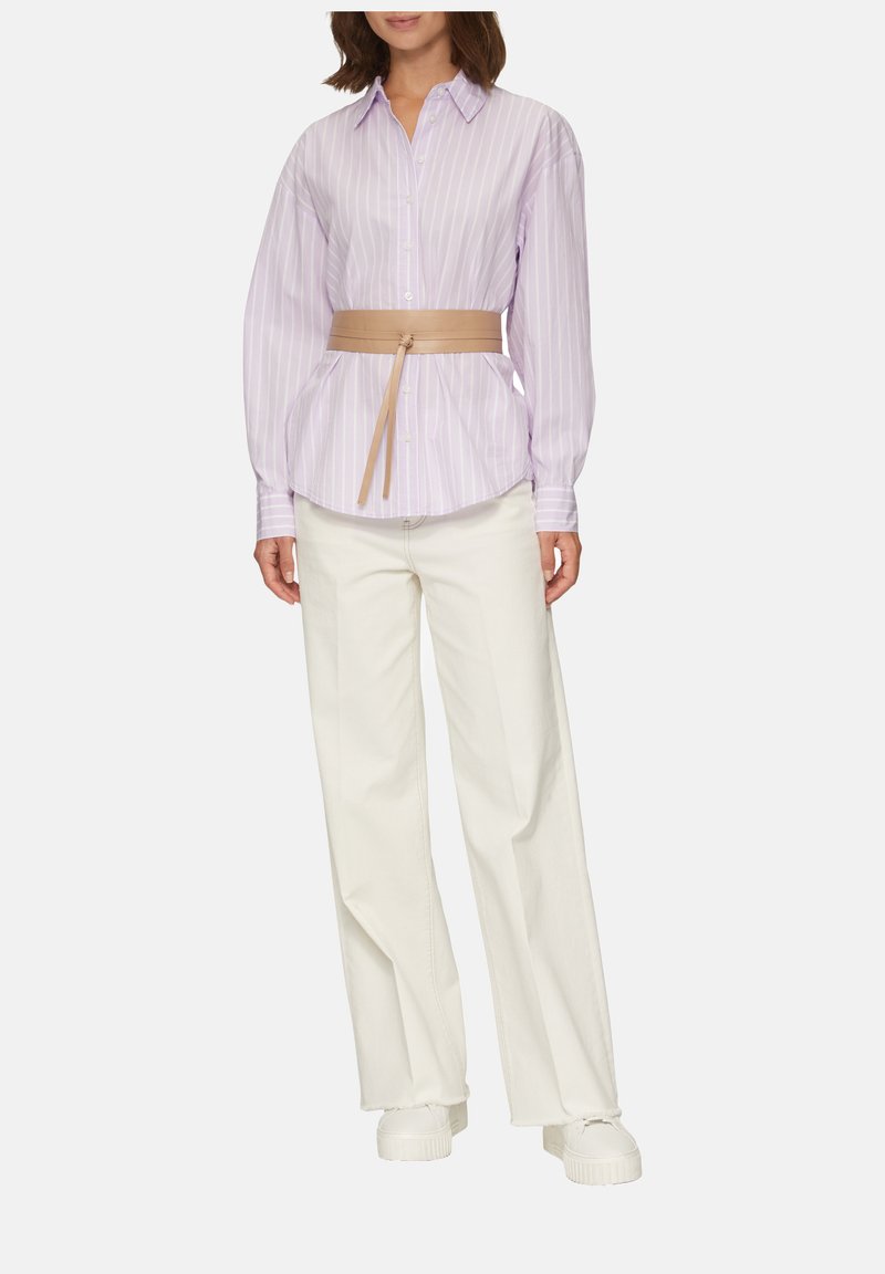 Helllila gestreifte Button-Down-Bluse mit einem gebundenen beigefarbenen Gürtel, kombiniert mit weiten weißen Hosen und klobigen weißen Sneakers, die geschichtete Texturen präsentieren.