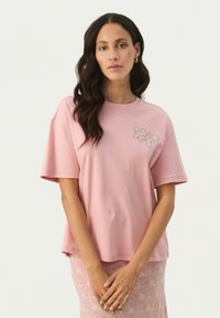 T-shirt en coton rose à manches courtes, avec un motif floral brodé sur la poitrine gauche. Texture douce et coupe décontractée.