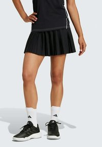 Mustaga volditud tenniseseelik, millel on must särk valgete aktsentidega, ja mustad spordijalatsid valgete sokkidega.