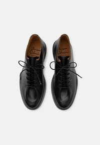 Black leather shoes with a smooth finish, round toe, and front lacing. Interior features tan leather lining and a branded insole.