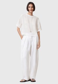 Vit linnetopp med korta ärmar och lös passform, kombinerad med vita plisserade vida byxor och silvriga flatsandaler. Enkel detalj med ett silverhalsband.