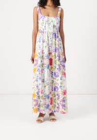 Blommig maxiklänning med fyrkantig halsringning och breda axelband. Har ett livfullt tryck av olika blommor i lila, gult och rött på en vit bakgrund.