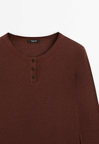 Bruine lange mouwen blouse met een ronde halslijn, drie knopen aan de voorkant en een zachte, textuurstof. Label zichtbaar bij de kraag.