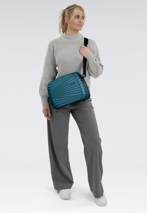 Borsa a spalla incrociata verde petrolio a righe con cerniera superiore, dettagli neri e tracolla regolabile. Presenta una forma strutturata e rettangolare.