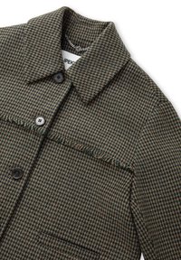 Brązowa i zielona kurtka w wzór houndstooth, z kołnierzykiem, dwiema czarnymi guzikami i frędzlami przy szwie.