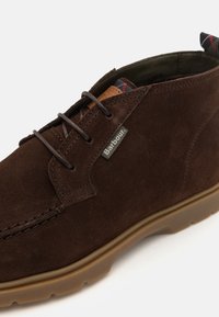 Stivale chukka in suede marrone con lacci marroni, linguetta in pelle a contrasto e suola in gomma. Presenta dettagli cuciti e etichetta con il logo Barbour.