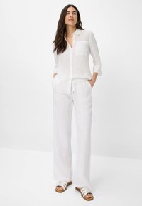 White linen button-up shirt with a chest pocket, paired with loose white linen pants. Accented with casual white sandals.