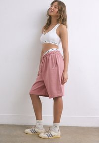 Shorts de survêtement rose clair avec une ceinture élastique, dotés de poches latérales et d'un logo brodé. Portés avec un bralette blanc et des baskets.