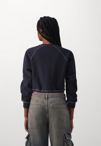 Sudadera navy recortada con mangas raglán y costuras visibles, combinada con pantalones cargo de mezclilla desgastados de talle alto con bolsillos.