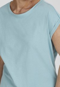 Light blue short-sleeve T-shirt with a round neckline, made of soft fabric. Features rolled cuffs and a relaxed fit. Smooth texture.