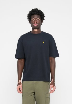 T-shirt en coton noir avec un col rond, des manches courtes, et un petit logo d'aigle jaune sur la poitrine gauche. Offre une coupe décontractée.