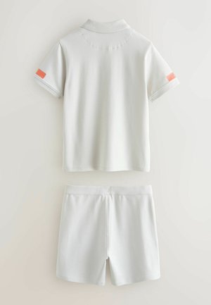 Witte polo met korte mouwen, voorzien van een koraalkleurig accent op de manchetten, gecombineerd met bijpassende witte korte broek, beide van gladde stof.