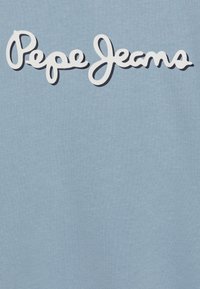 Světlomodrá tkanina se výrazným bílým vyšitým logem, které zní "Pepe Jeans" v kurzívě. Hladká textura, stručný design.