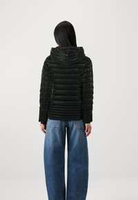 Svart pufferjakke med hette, med horisontalt quiltet mønster og en tilpasset design, kombinert med løse blå jeans.